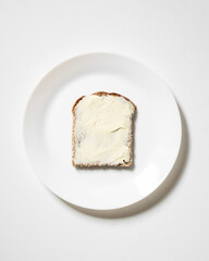 Slice of whole wheat bread, toast with butter and cream cheese on white plate. Breakfast, snack, sandwich, lunch with spread. Dark rye bread. Copy space. Flat lay.