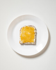 Toast with butter or cream cheese and jam, jelly on white plate. Slice of bread with sweet spread. Breakfast, snack, sandwich, lunch. Dark rye whole wheat bread. Copy space. Flat lay.