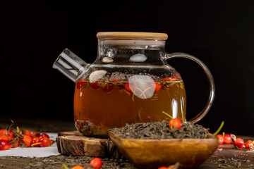 red rosehip fruits and hot green tea in a transparent teapot