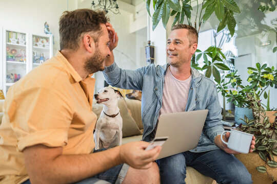 Gay couple shopping online with credit card and laptop at home with dog