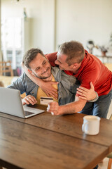 Obraz premium Gay couple hugging and shopping online with credit card and laptop
