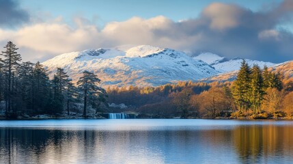 Fototapeta premium Snowy mountains reflect in calm lake at sunrise with trees and clouds creating a beautiful landscape view in nature.