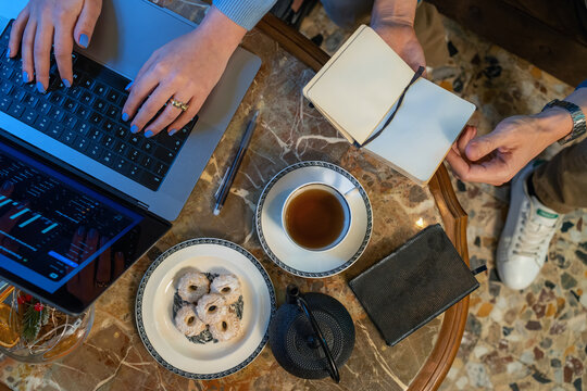 Hands typing on laptop with tea and cookies on marble table in cozy workspace