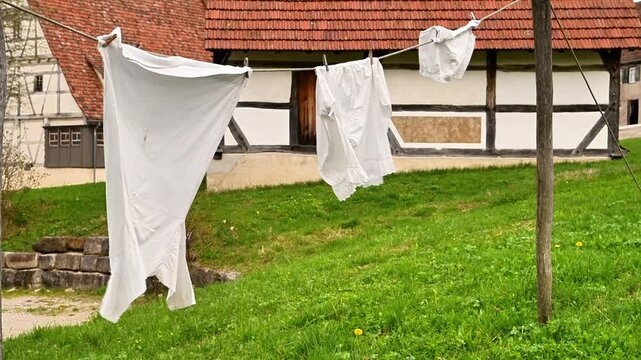 Row of ancient clothes is hanging on a clothesline outside. The clothes are freshly washed and are drying in wind. Shirt Underpants and bra in slow motion