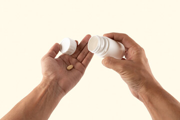 Male hands holding a pill from a white medicine bottle isolated on light yellow background