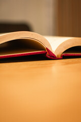 Close-Up of an Open Islamic Book with Red Binding on Wooden Surface with Bokeh Background