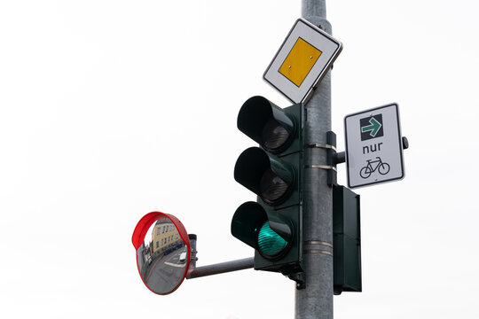 A traffic light showing green, with a bicycle sign indicating a bike path. A mirror reflects the surroundings, hinting at a busy urban area.