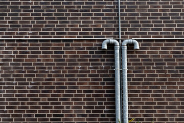 Two metal pipes extend vertically from a brick wall, showcasing a textured surface of reddish-brown bricks in a city setting on a clear day.