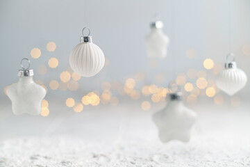 White christmas ornaments of various shapes hanging against a light background with soft, warm...