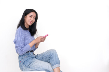 Side view: A young woman sitting on a wooden bench while holding a mobile, looking forward with a smiling, happy expression