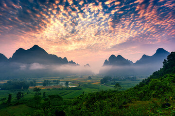 Obraz premium Landscape of vibrant sunrise over mountain range with foggy, river and traditional village in Phong Nam Valley