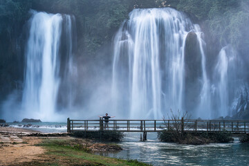 Ban Gioc Waterfall flowing with male tourist standing on wooden bridge