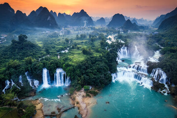 Sunset over mountain range with Ban Gioc waterfall flowing in tropical rainforest at Vietnam