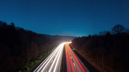 A long exposure shot of a highway at night, with light trails on the road and trees on either side. In the background, there are hills and a starry sky. Wallpaper, banner.