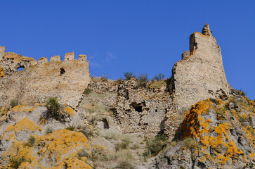 A stunning view of ancient stone ruins perched on a rocky hillside, partially covered with vibrant...