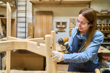 Young woman working with power tools in a woodworking workshop