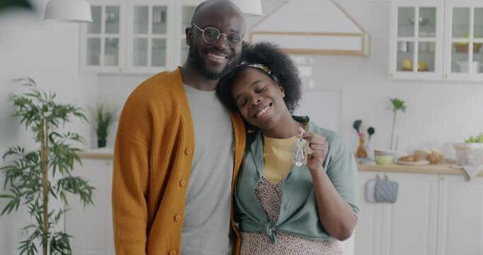 Slow motion portrait of happy African American couple man and woman standing in new house holding keys smiling looking at camera. Real estate and relocation concept.