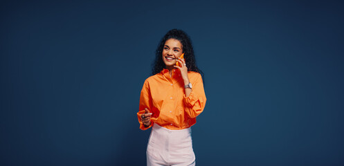 Woman engaging in communication on mobile phone with bright orange and blue color blocking background