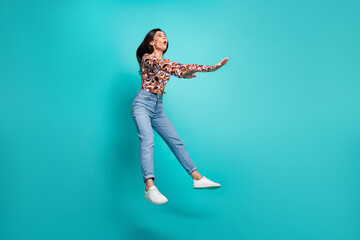 Full length photo of shocked lovely girl wear print shirt jumping high empty space isolated turquoise color background