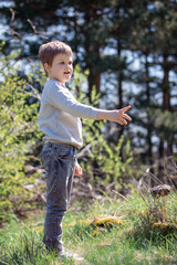 A cheerful, playful boy during a walk in the summer forest, the child sees something and points with his finger