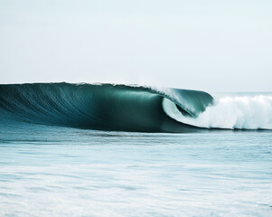 Majestic ocean wave curling gracefully at sunrise along a tranquil shoreline with soft waves in the background