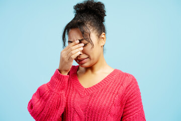 Young woman crying and touching her face on blue background