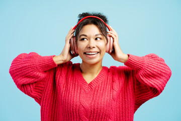Young woman enjoying music with wireless headphones on blue background
