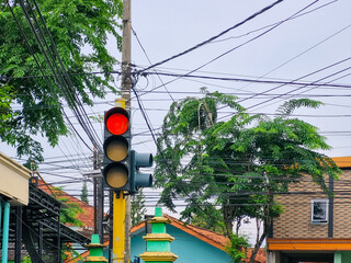 Red traffic light with trees and cables in the background on the highway of Pamekasan city, Madura,...
