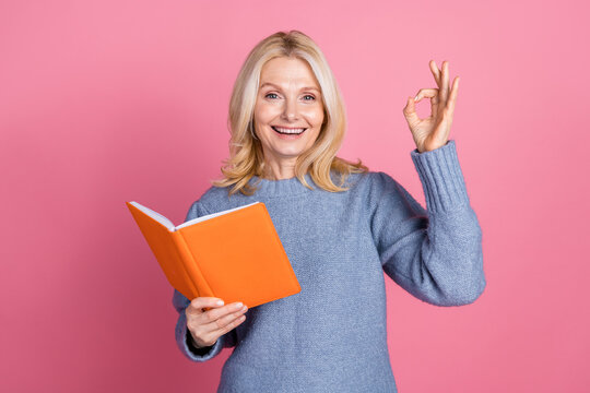 Photo portrait of attractive senior woman read book show okey dressed stylish blue knitted clothes isolated on pink color background