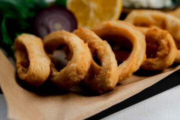 crispy fried calamari rings , golden brown crusty finger food served with dip sauce, greens and lemon, styled on plate with cooking paper