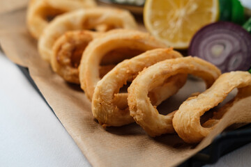 crispy fried calamari rings , golden brown crusty finger food served with dip sauce, greens and lemon, styled on plate with cooking paper