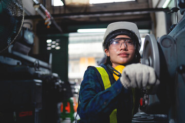 A woman wearing a hard hat and safety glasses is working on a machine. She is focused on her task and she is in a serious mood
