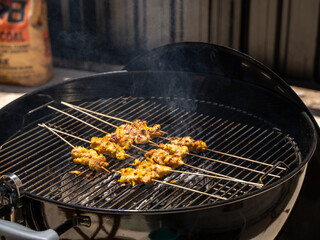 Grilling skewered meat on a smoky charcoal barbecue in bright sunlight