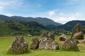 English Heritage Castlerigg Stone Circle of 5000 years old near Keswick, UK in the Lake District National Park on a hill overlooking surrouning hills and mountains against a white clouded blue sky
