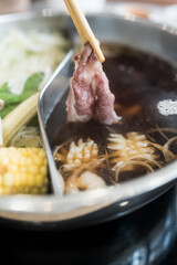Man holding slice beef out from hot pot shabu shoyu soup base by chopsticks with steam