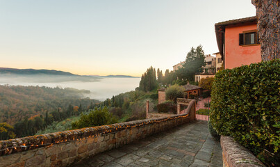 Cobbled street overlooking foggy valley in tuscany at dawn