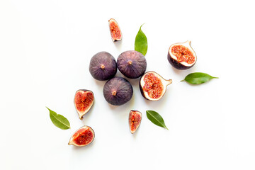 Whole and cut fresh figs with green leaves on white background. Top view