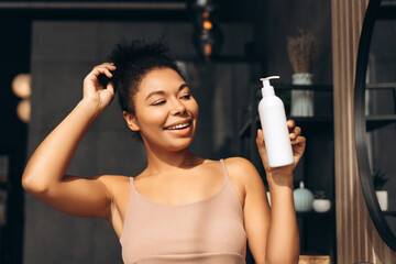 Happy young woman holding cosmetic product touching her hair