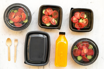 Tomatoes salad in lunch boxes with orange juice in a bottle and disposable cutlery, top view