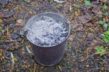 one old brown enamel bucket full of grey ash and soot stands on the ground on an autumn street © butus