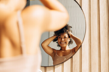 Woman styling her afro hair in front of mirror at home