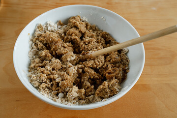 Making gingerbread. A bowl of flour and dry ingredients is being mixed with a buttery, spiced liquid from a saucepan. A wooden spoon rests in the bowl for stirring.