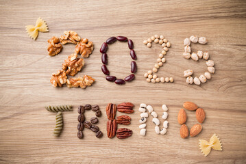 2025 trend alphabet made from walnut, red bean, soybean, chickpea, pasta, coffee bean, pecan, black eyed pea and almond on wooden background