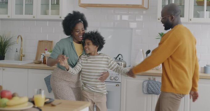 African American family mother father and kid dancing having fun fooling around in kitchen in apartment. Modern lifestyle and entertainment concept.
