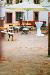 Outdoor Event Setup in Garden Area with Benches, Large Umbrella, and Decorated Table