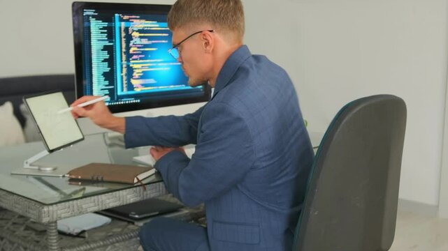 Developer analyzes code on computer, optimizing tasks with tablet.