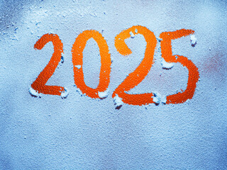 Hand written sign 2025 on glass covered with snow with blue cast and warm orange color in the...