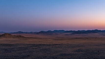 Fototapeta premium Expansive desert landscape at dusk with fading light and distant mountains in the horizon