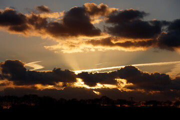 Dramatic sunset sky with golden light breaking through dark clouds.  Silhouetted trees line the horizon.