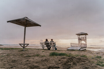 Backview of two adult guys, sitts on the bench and spending time by look around on the beauty of lake